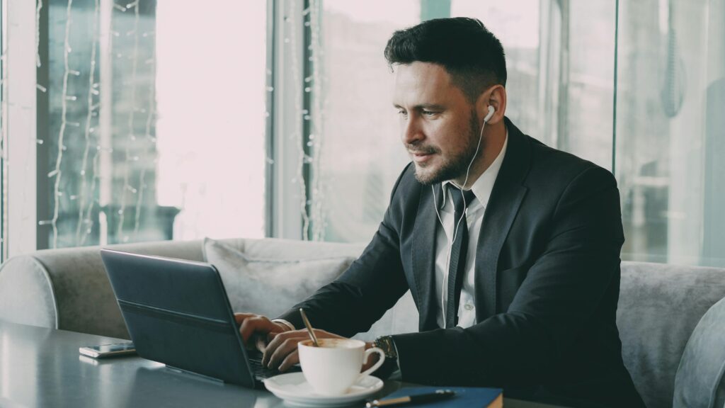 Business professional using a laptop in a cafe, wearing earbuds.