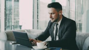 Business professional using a laptop in a cafe, wearing earbuds.